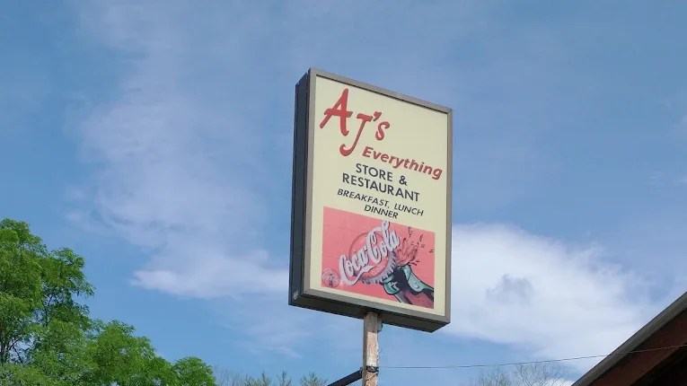 Sign for AJ's Everything Store & Restaurant, advertising breakfast, lunch, and dinner with a Coca-Cola graphic.